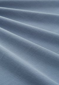 Hellblauer Stoff mit strukturierter Oberfläche, der subtile Falten und eine glatte Oberfläche zeigt, geeignet für Kleidung oder Polster.