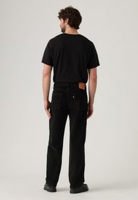 Zwarte corduroy broek met rechte pijpen, voorzien van een leren achterpatch en twee achterzakken. Gedragen met een shirt in effen zwart en schoenen.