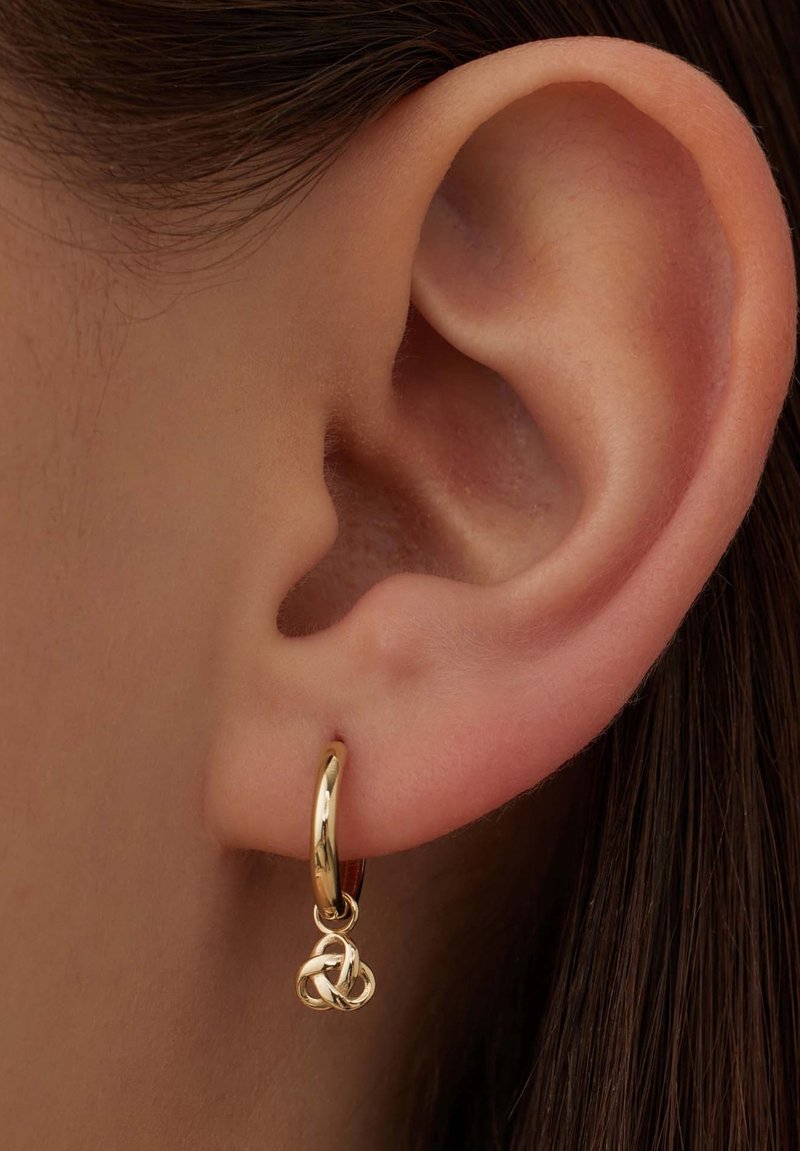 Gold hoop earring with a small intertwined knot pendant, featuring a smooth, glossy finish. Worn on the lobe of a pierced ear.