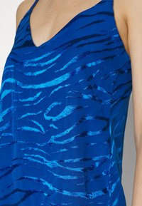 Top sem mangas azul com um padrão ondulado em diferentes tons de azul. O tecido tem uma textura brilhante e um design de decote em V.