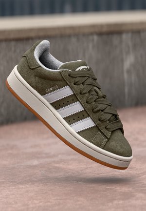 Olivgrüner Veloursleder-Sneaker mit weißen Streifen, beiger Mittelsohle, Gummiaußensohle, geschnürten Schnürsenkeln und dem Wort „CAMPUS“ an der Seite.