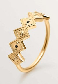 Anillo geométrico dorado con acentos cuadrados y piedras negras. La textura suave, el diseño en zigzag y el acabado pulido realzan su atractivo visual.