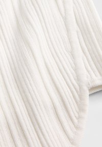 Hvid tekstureret stof med bølgende ribbet design. Materialet virker blødt og fyldigt med en glat kantdetalje. Velegnet til forskellige tekstilformål.