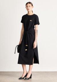 Μαύρο φόρεμα με κοντά μανίκια, λεπτομέρεια με κόμπο στη μέση, πλαϊνές σκισμές και χρυσές λεπτομέρειες. Συνδυασμένο με μαύρες γόβες μυτερές και μίνι τσάντα.