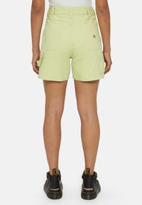 Lys grønne cargo shorts med flere lommer, høj talje og en glat tekstur, parret med sorte støvler med spænder.