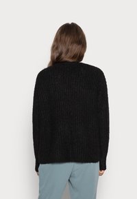 Maglione nero lavorato a maglia con una vestibilità rilassata, caratterizzato da una texture a coste e un colletto rotondo, abbinato a pantaloni azzurri chiari.