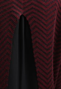 Vestito bordeaux e nero con un motivo a zig zag, caratterizzato da un tessuto lavorato sulla parte superiore e da un tessuto liscio sulla parte inferiore, creando un contrasto.