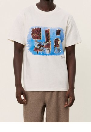 T-shirt en coton blanc avec un imprimé coloré de meubles abstraits sur fond bleu, à manches courtes et coupe décontractée.