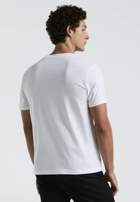 Witte T-shirt met korte mouwen en een ronde hals, gemaakt van een gladde stof. Heeft een eenvoudig ontwerp zonder zichtbare logo's of patronen.