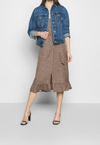 Denim jacket with button closure, blue wash. Below, a brown dress with a leopard print, frill hem, and front slit. Black high-heeled sandals.