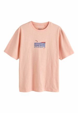 Lichtroze T-shirt met een kleine afbeelding van een persoon die in blauw water en rood land duikt, de tekst luidt "IN TO THE WATER I GO."