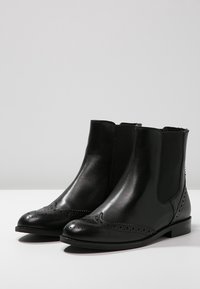 Botas de tobillo de cuero negro con un acabado suave, paneles laterales elásticos, detalles de brogue en la punta y un tacón bajo en bloque.