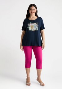 Camiseta de manga corta de color marino con un gráfico floral y el texto "TAKE IT EASY". Combinada con pantalones cortos de color rosa vibrante y tacones con tiras.