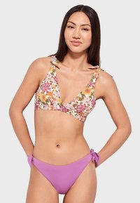 Top de bikini floral con escote en V y tirantes de lazo; presenta parte inferior de bikini en color sólido morado con acentos de lazo en los lados.