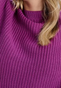 Fialový pletený svetr se širokým žebrovaným výstřihem a strukturovanou tkaninou. Pletený vzor má vertikální řady, které dodávají designu hloubku.