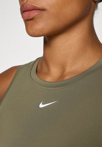 Olivovo zelený športový top s okrúhlym výstrihom a bielym logom Nike na hrudi. Hladká textúra a priliehavý strih.