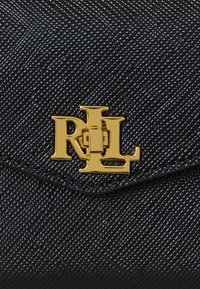 Sac à main en tissu texturé noir avec un accent doré portant les initiales "RL" et un détail de fermoir. Le matériau présente un motif tissé.