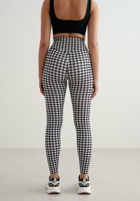 Czarno-białe legginsy w jodełkę z wysokim stanem, zestawione z czarnym krótkim topem i sportowymi trampkami. Gładka faktura, dopasowany krój.
