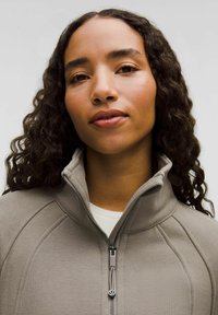 Grå zip-up jakke lavet af tekstureret stof med høj krave og syninger, der har en sølvfarvet lynlås og rund træk-tab.