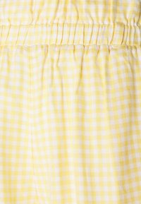 Žlutá a bílá kostkovaná látka s nařaseným elastickým pasem a sklady.