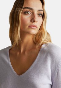 Sweter w kolorze lawendowym z dekoltem w serek o miękkiej teksturze, charakteryzujący się luźnym krojem i widocznymi szwami na ramionach.