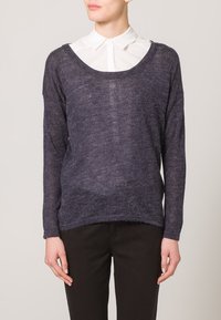 Maglione leggero navy a maglia con scollatura larga, maniche lunghe e vestibilità leggermente ampia, indossato sopra una camicia bianca con colletto.