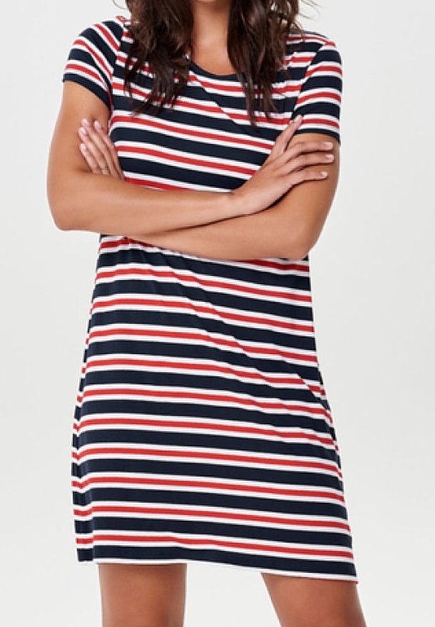 Femme portant une robe courte à manches courtes avec des rayures horizontales bleu marine, rouge et blanc, debout les bras croisés.