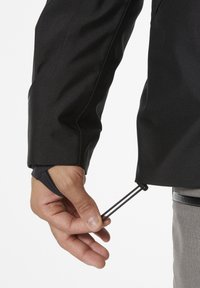 Czarna wodoodporna kurtka z teksturowanym wykończeniem. Regulowany sznurek u dołu, ściągany ręcznie, podkreślający funkcjonalność projektu.