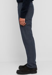 Pantaloni a quadri blu navy realizzati in tessuto intrecciato, con vestibilità slim e motivo a quadretti discreto. Abbinati a stivaletti neri elasticizzati alla caviglia.