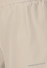Beige Sportshorts aus leichtem Material mit elastischem Bund. Mit einer glatten Textur und dem Aufdruck "ENDURANCE" in Grau.