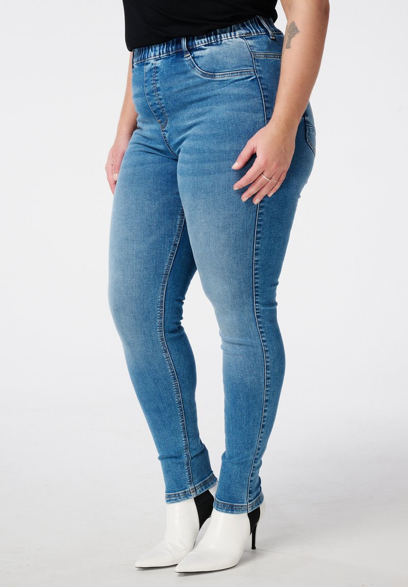 Strakke blauwe jeans van denim, met een hoge tailleband en een gladde, licht vervaagde textuur. Draagt met puntige witte hakken.