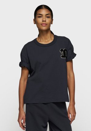 T-shirt in cotone navy con maniche arrotolate, dotato di un numero "10" ricamato in bianco e nero sul lato sinistro del petto. Taglio semplice e rilassato.