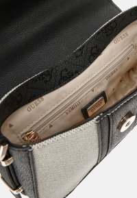 Sac à main noir et gris clair en cuir et textile. L'intérieur comporte une poche zippée et un motif de marque beige. Accents en matériel doré.