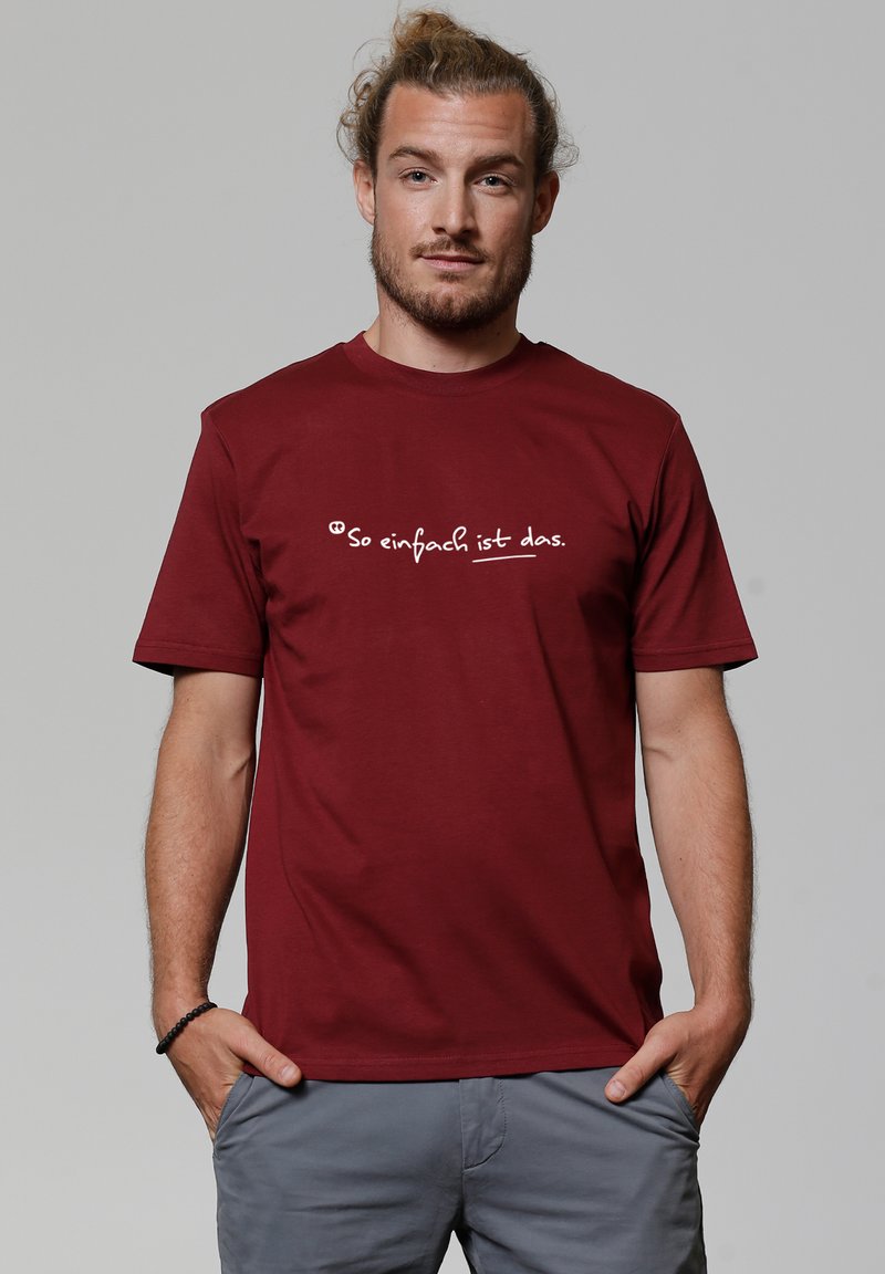 T-shirt en coton bordeaux avec un design graphique blanc au texte "So einfach ist das" sur la poitrine, manches courtes et col rond.