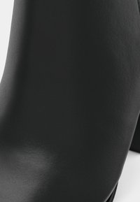 Bottine noire à talons hauts en cuir texturé, présentant une silhouette élégante et une finition lisse avec un design de talon partiellement visible.