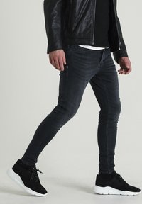 Vaqueros negros ajustados con un desvanecimiento sutil, combinados con zapatillas de ante negras que tienen una suela blanca. La chaqueta de cuero añade textura y contraste.
