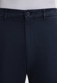 Pantaloni blu navy con una texture liscia, chiusura a bottone e un motivo sottile. Comprende un discreto accento con logo vicino alla vita.