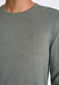 Grüner Pullover mit Rundhalsausschnitt, gestrickter Textur und einem kleinen gestickten Logo auf der Brust. Verfügt über gerippte Bündchen und Saum.