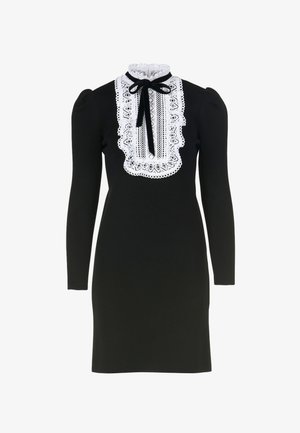 Abito nero a maniche lunghe realizzato in tessuto texturizzato, con colletto in pizzo bianco e dettaglio a fiocco. Silhouette aderente con spalle a sbuffo.