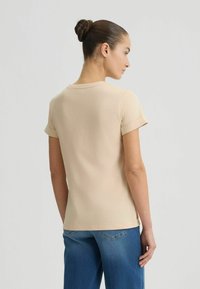 Lichtbeige t-shirt met korte mouwen, ronde halslijn en omgeslagen mouwen. Zachte stof met een strakke snit, gecombineerd met blauwe jeans.