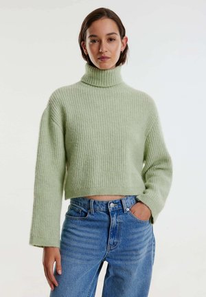 Hellgrüner, taillierter Rollkragenpullover mit gerippter Textur, kombiniert mit hochgeschnittenen hellblauen Denim-Jeans. Schlichtes, modernes Design.