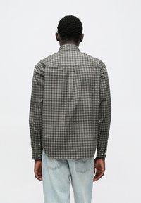 Camicia a quadri scura con bottoni, colletto a punta e maniche lunghe, caratterizzata da diverse tonalità di grigio, nero e bianco in un motivo a scacchi.