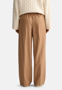 Pantalones marrones de pierna ancha con pliegues, confeccionados en una tela suave. Cintura elástica y puños de color claro acanalados en los tobillos.