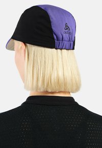 Schwarze und lila Kappe mit gebogenem Schirm und elastischem Rücken. Merkmale sind ein Logo auf der Rückseite, leichtes Material und eine glatte Textur.