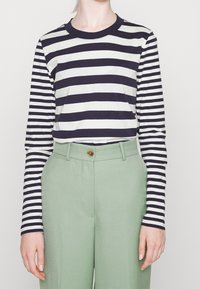 Camicia a maniche lunghe a righe in cotone navy e bianco, abbinata a pantaloni alla vita alta in verde menta con chiusura a bottone.