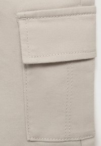 Beige tygficka med lock, sömnadsdetaljer, rektangulär form och lätt struktur, placerad på ett plagg.