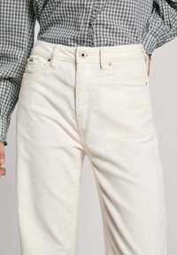 Pantalones de pana blancos con corte recto, que cuentan con dos bolsillos, cierre de botón en la parte superior y una suave textura de estría vertical.