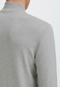 Maglione grigio a maglia con colletto alto, caratterizzato da una texture liscia e un design aderente. Presenta lievi dettagli di cuciture vicino alla spalla.