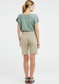 Zelený krátky rukáv s textúrovaným dizajnom, doplnený béžovými šortkami s prednými a zadnými vreckami, nosený s viacfarebnými športovými topánkami.