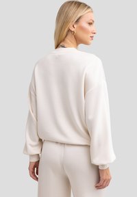 Sudadera de color beige claro, de corte grande, con escote redondo y hombros caídos. Textura suave y ajuste relajado, combinada con pantalones a juego.